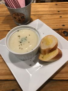 De Bois bowl of mushroom soup with two pieces of garlic bread on a white square plate